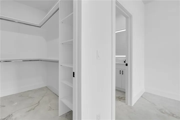 Walk-in closet with built-in shelving, chrome hanging rods, and marble-look flooring