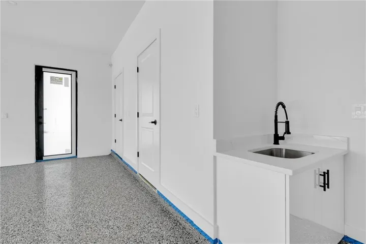 Polished aggregate flooring, white base cabinetry with black hardware, undermount stainless steel sink, black gooseneck faucet, and a solid surface countertop