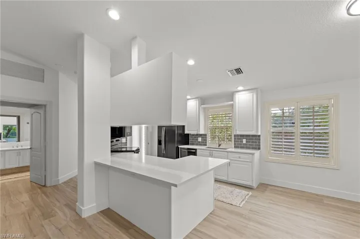 Kitchen featuring backsplash, a peninsula, light wood finished floors, white cabinets, and light stone countertops