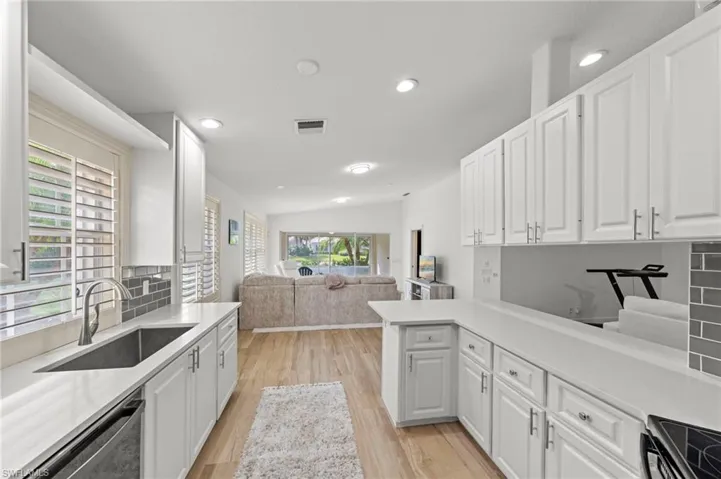 Kitchen featuring white cabinetry, open floor plan, vaulted ceiling, dishwasher, and light wood-type flooring
