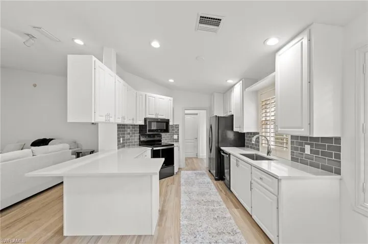 Kitchen with white cabinets, black appliances, a peninsula, light wood-style floors, and decorative backsplash