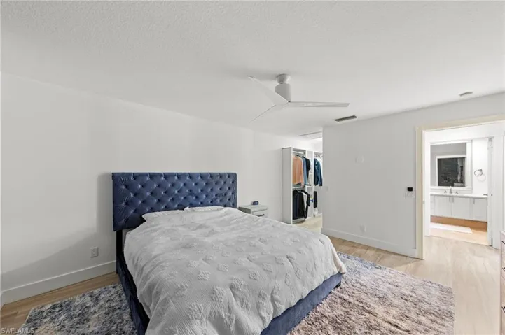 Bedroom with light wood-style flooring, a textured ceiling, a walk in closet, and a ceiling fan