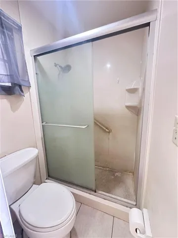 Bathroom with tile patterned floors, a shower stall, and toilet