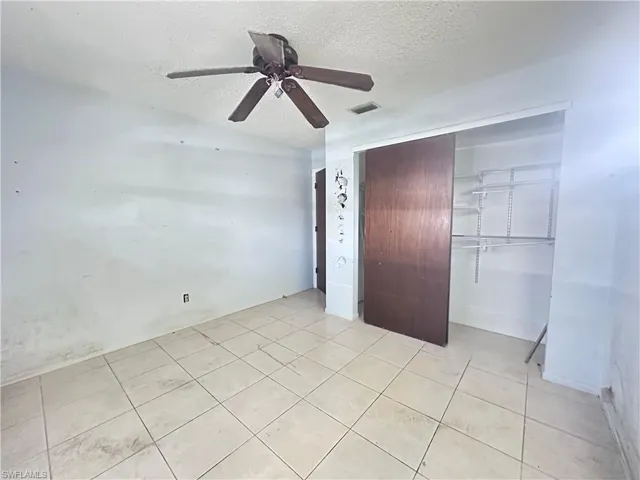 Unfurnished bedroom with a textured ceiling, a closet, a ceiling fan, and light tile patterned floors