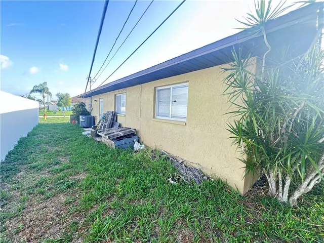 View of side of home featuring stucco siding, central AC, and a yard