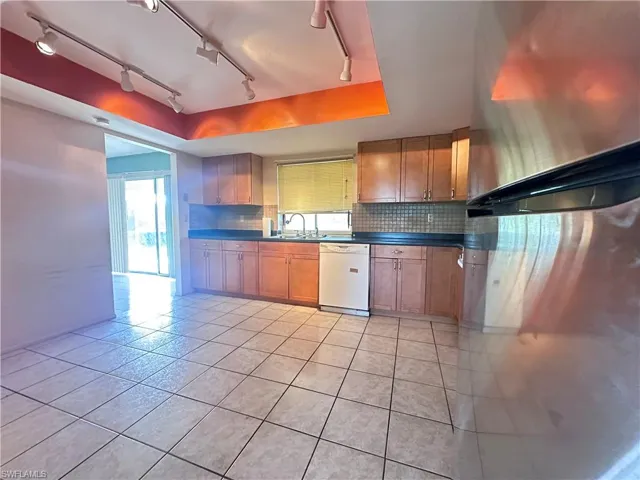 Kitchen featuring freestanding refrigerator, white dishwasher, light tile patterned flooring, track lighting, and decorative backsplash