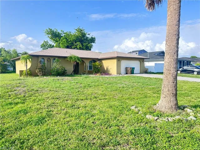 Ranch-style house with stucco siding, driveway, a front lawn, and an attached garage