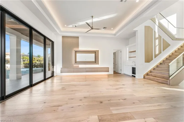 Unfurnished living room with light wood-type flooring, a tray ceiling, a ceiling fan, and beverage cooler