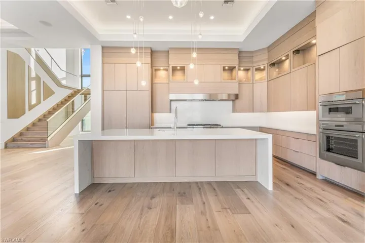 Kitchen featuring a raised ceiling, modern cabinets, light wood finish cabinets, light stone countertops, and pendant lighting