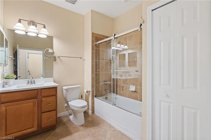 Full bathroom with tile patterned floors, shower / bath combination with glass door, vanity, and toilet