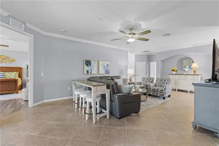 Tiled living room featuring ceiling fan and ornamental molding