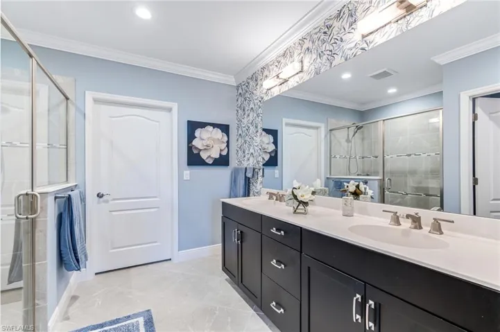 Full bathroom with double vanity, a sink, a stall shower, and crown molding
