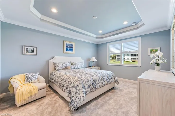 Bedroom featuring a raised ceiling, light carpet, and crown molding