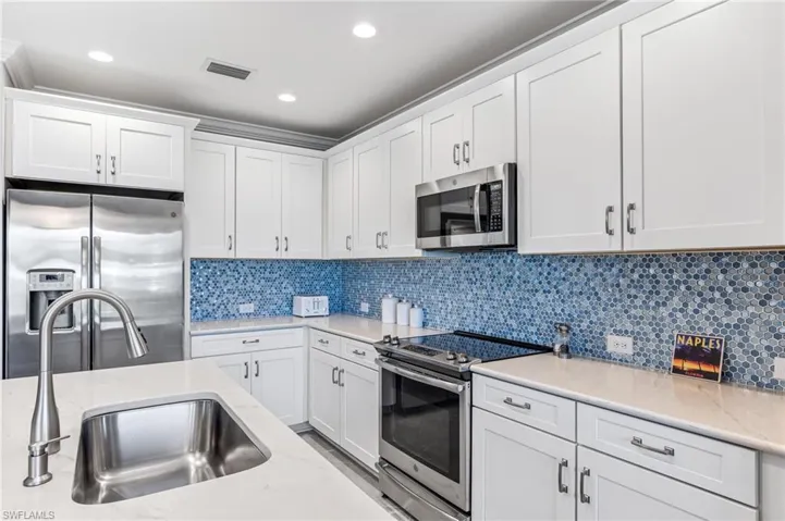 Kitchen with tasteful backsplash, appliances with stainless steel finishes, a sink, and white cabinetry