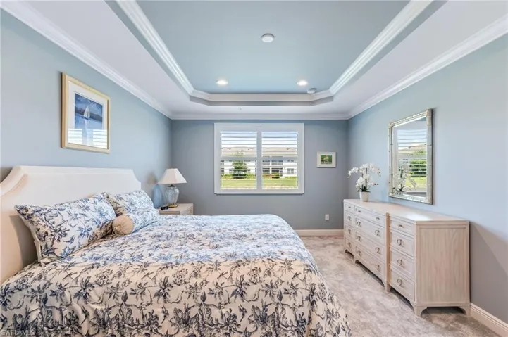 Bedroom featuring ornamental molding, multiple windows, a raised ceiling, and light carpet
