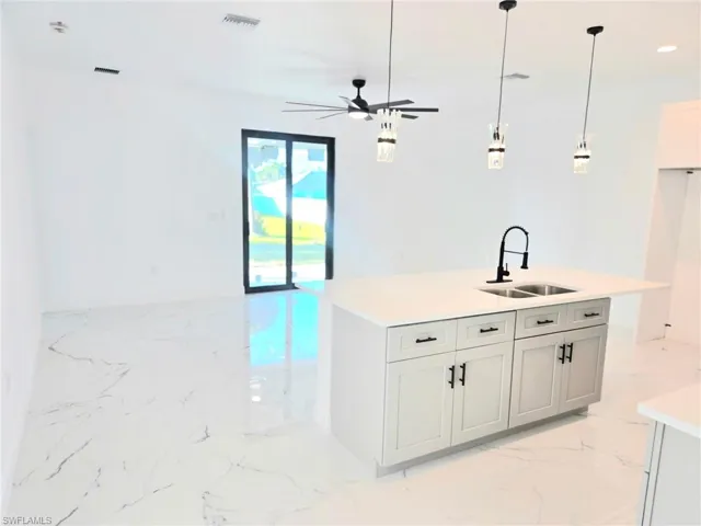 Kitchen featuring light marble finish flooring, a kitchen island with sink, hanging light fixtures, a ceiling fan, and light stone countertops