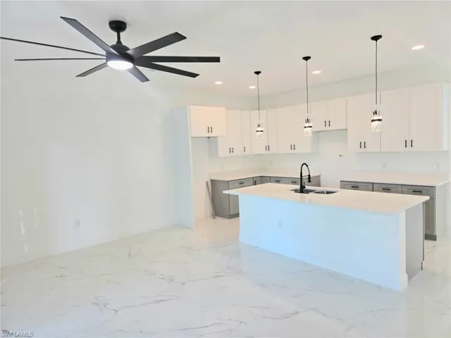Kitchen with light marble finish flooring, white cabinetry, an island with sink, recessed lighting, and hanging light fixtures