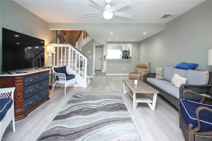 Living room with light wood-style floors, ceiling fan, visible vents, stairs, and baseboards