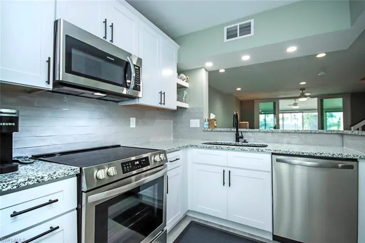Kitchen featuring white cabinetry, open shelves, visible vents, stainless steel appliances, and a sink