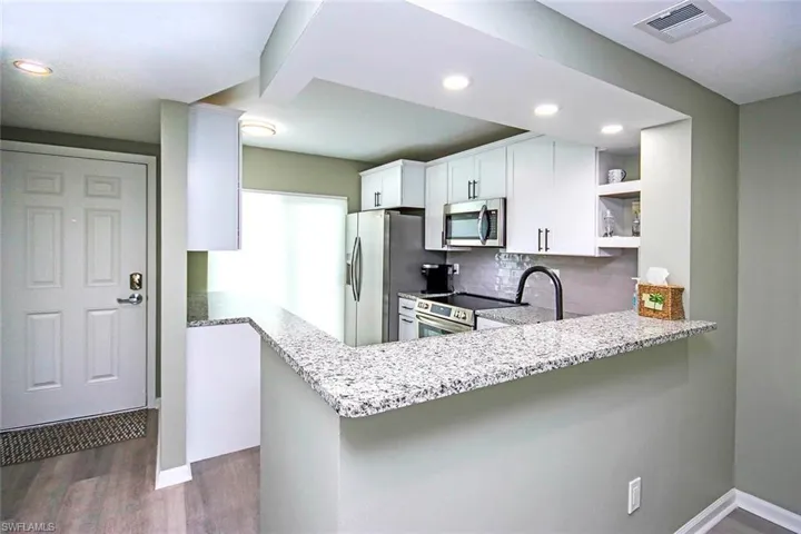 Kitchen with light stone counters, open shelves, visible vents, stainless steel appliances, and a sink