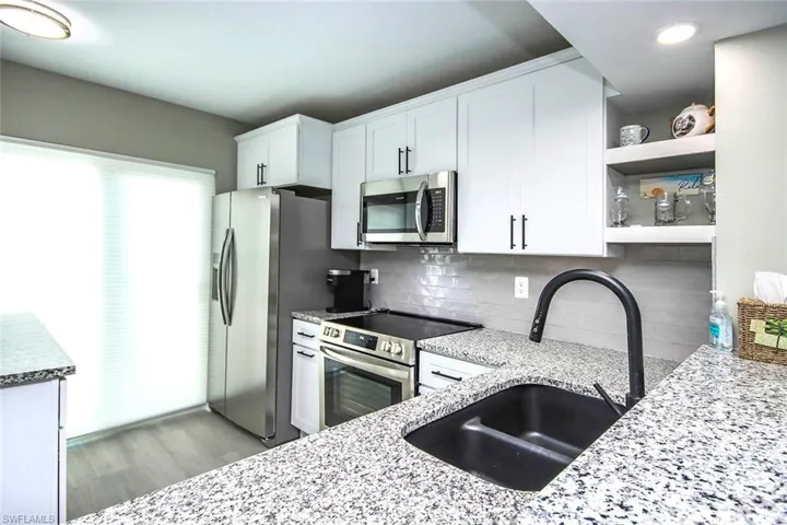 Kitchen with light stone countertops, light wood-style flooring, white cabinetry, appliances with stainless steel finishes, and a sink
