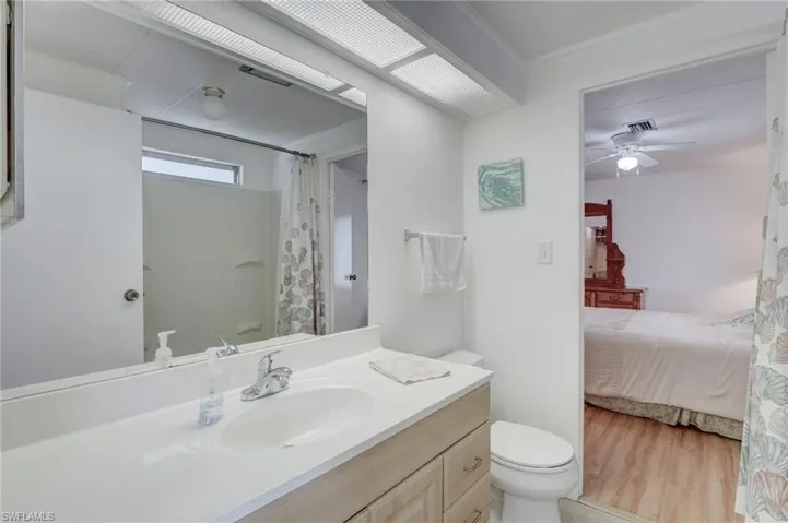 Ensuite bathroom with a shower with shower curtain, vanity, ceiling fan, crown molding, and light wood finished floors