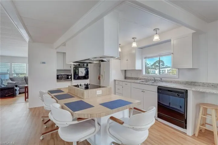 Kitchen featuring a kitchen bar, white cabinets, light countertops, black appliances, and light wood-type flooring