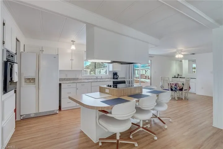 Kitchen with light countertops, white cabinets, white fridge with ice dispenser, a kitchen bar, and light wood-style flooring