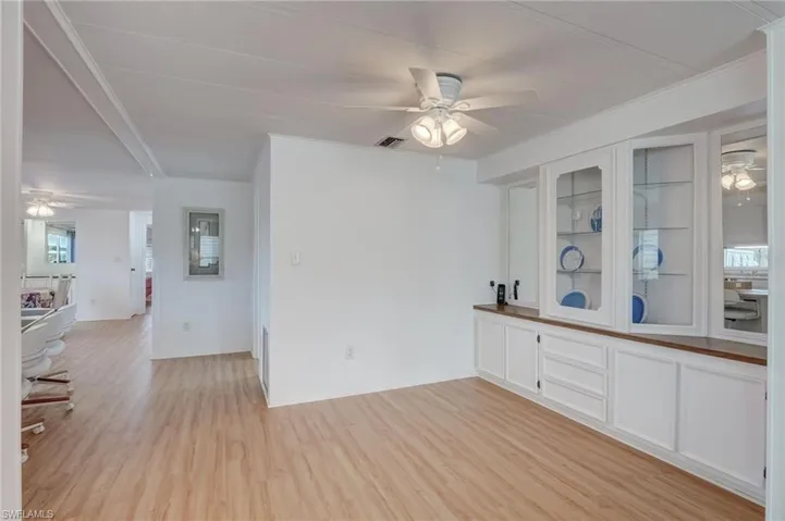 Bar area with ceiling fan, white cabinetry, glass insert cabinets, light wood-style flooring, and ornamental molding