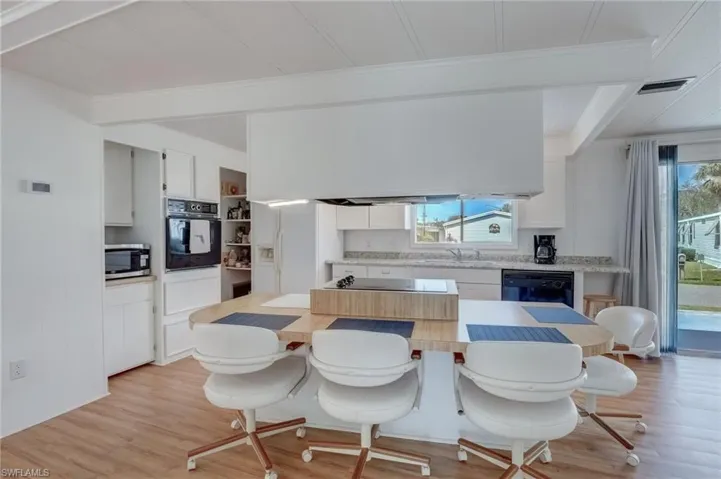 Kitchen featuring white cabinetry, beamed ceiling, black appliances, light wood-style floors, and crown molding