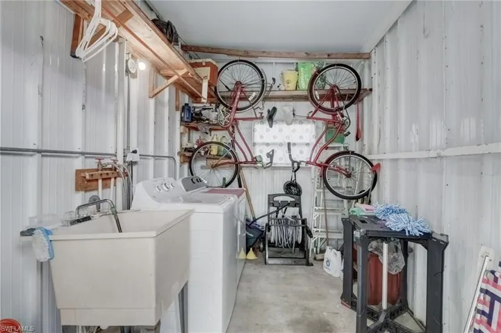 Laundry room featuring concrete flooring, metal wall, and washing machine and clothes dryer