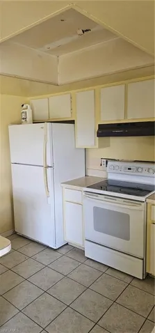Kitchen featuring stove, range hood, refrigerator, light tile patterned floors, and light countertops