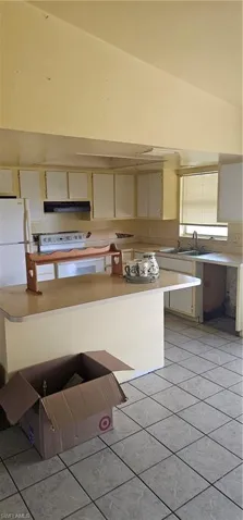 Kitchen featuring cream cabinets, extractor fan, light tile patterned floors, light countertops, and high vaulted ceiling