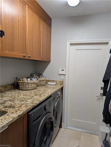 Laundry area with a textured ceiling, washer and clothes dryer, light tile patterned flooring, and cabinets