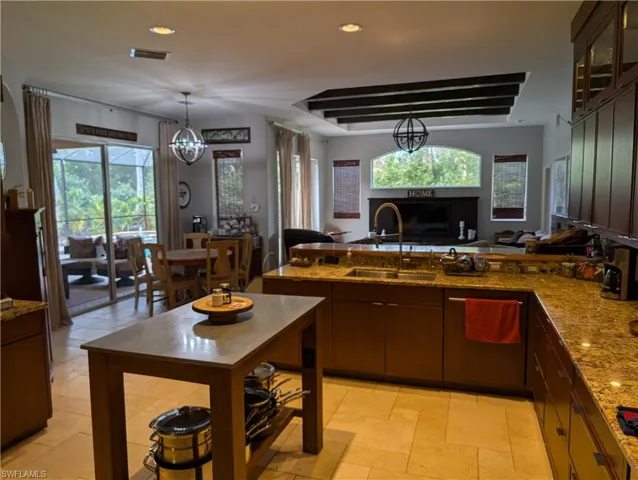 Kitchen with light stone counters, an inviting chandelier, sink, dark brown cabinetry, and decorative light fixtures