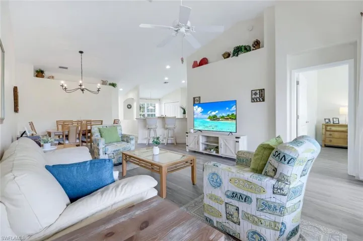 Living area featuring high vaulted ceiling, wood finished floors, a chandelier, and a ceiling fan