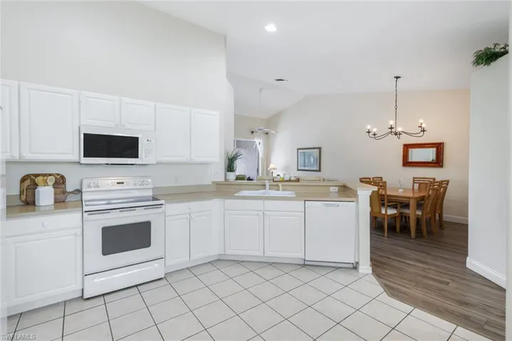 Kitchen featuring white appliances, a chandelier, a peninsula, light countertops, and white cabinetry