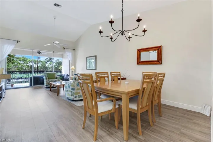 Dining room with ceiling fan, light wood-style flooring, a chandelier, and high vaulted ceiling