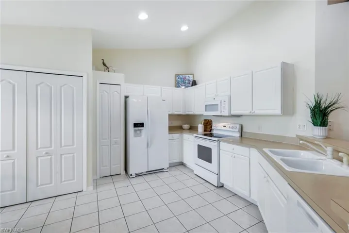 Kitchen featuring white appliances, light tile patterned flooring, white cabinetry, a towering ceiling, and light countertops