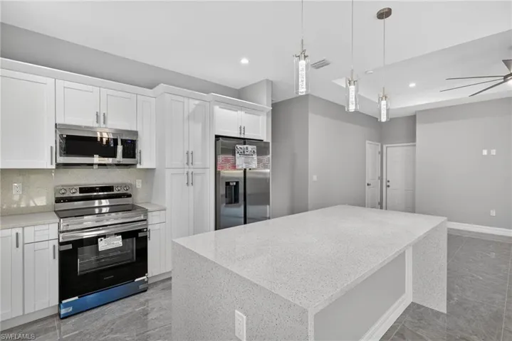 Kitchen with stainless steel appliances, white cabinetry, decorative light fixtures, a kitchen island, and light stone counters
