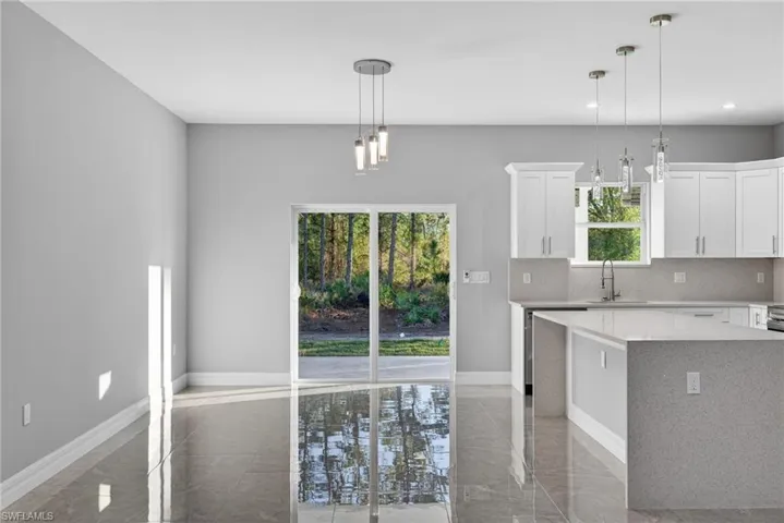 Kitchen with light stone counters, white cabinets, hanging light fixtures, and a kitchen island