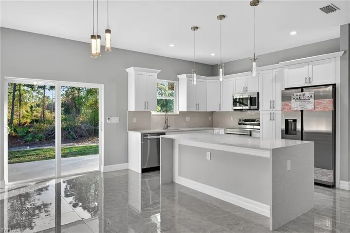 Kitchen featuring stainless steel appliances, light stone counters, a kitchen island, white cabinets, and light marble finish floors