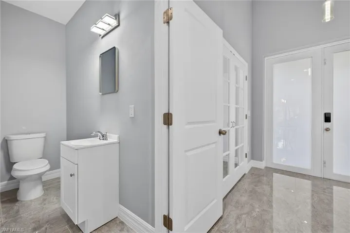 Half bath featuring vanity, french doors, and light marble finish flooring