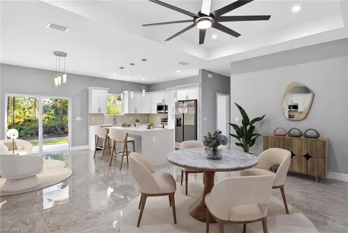 Dining space with a raised ceiling, a ceiling fan, light marble finish floors, and recessed lighting