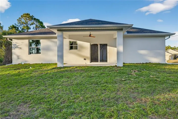 Back of property featuring ceiling fan, stucco siding, a yard, a patio area, and a shingled roof