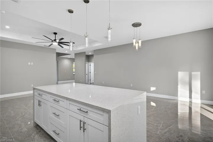 Kitchen with white cabinetry, marble tiled flooring, pendant lighting, open floor plan, and a ceiling fan