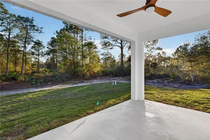View of grassy yard featuring ceiling fan, a patio, and view of wooded area