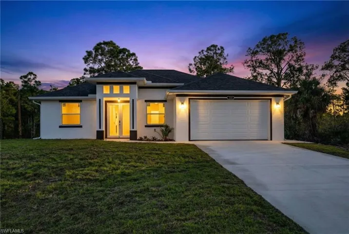Prairie-style home with stucco siding, concrete driveway, a front yard, an attached garage, and roof with shingles
