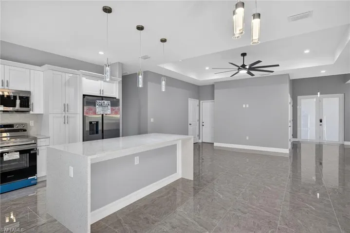 Kitchen featuring stainless steel appliances, hanging light fixtures, a tray ceiling, white cabinets, and recessed lighting