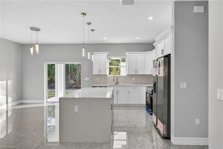 Kitchen with pendant lighting, stainless steel fridge, light stone counters, white cabinets, and light marble finish floors